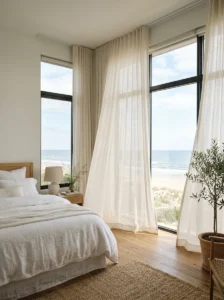 Bright coastal bedroom with oversized windows and flowing white sheer curtains.