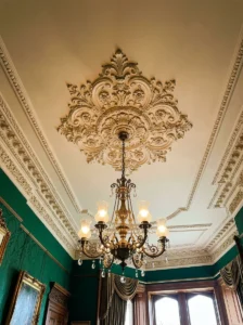 Victorian living room ceiling with an ornate medallion, chandelier, and crown molding.