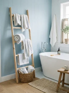 Wooden ladder rack displaying rolled white and blue-striped towels in a coastal bathroom.