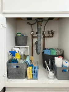 Under-sink baskets organizing cleaning supplies around kitchen plumbing.