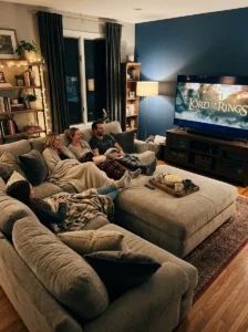 Large upholstered ottoman providing comfortable footrest space in a cozy TV room.